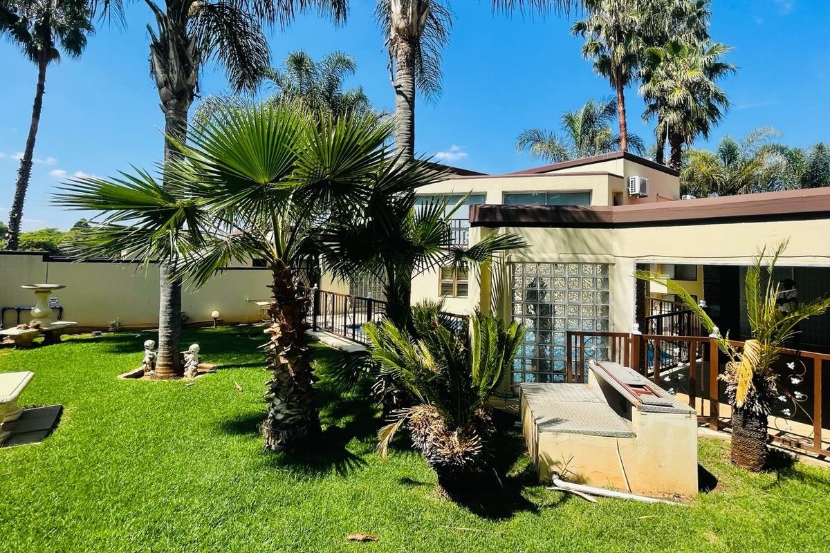 Rear exterior view featuring a landscaped garden, built-in braai area, timber decking, and a distinctive glass block feature wall.