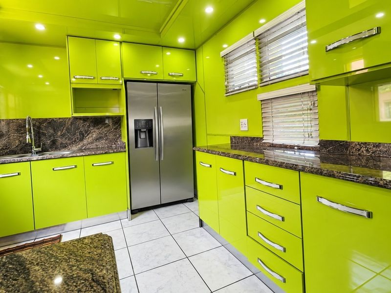 Modern kitchen featuring vibrant high-gloss lime green cabinetry, granite countertops, stainless steel appliances, and tiled flooring with recessed lighting.