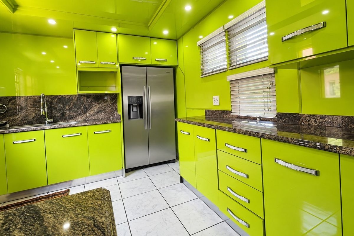 Modern kitchen featuring vibrant high-gloss lime green cabinetry, granite countertops, stainless steel appliances, and tiled flooring with recessed lighting.