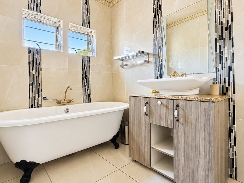 A well-appointed bathroom featuring a classic freestanding bathtub, a modern vanity with a vessel sink, and decorative mosaic tile accents.