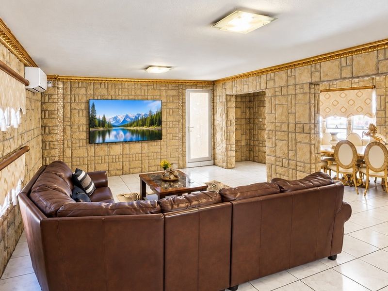 Spacious open-plan living and dining area featuring distinctive stone-clad walls, tiled flooring, and decorative gold crown molding throughout.