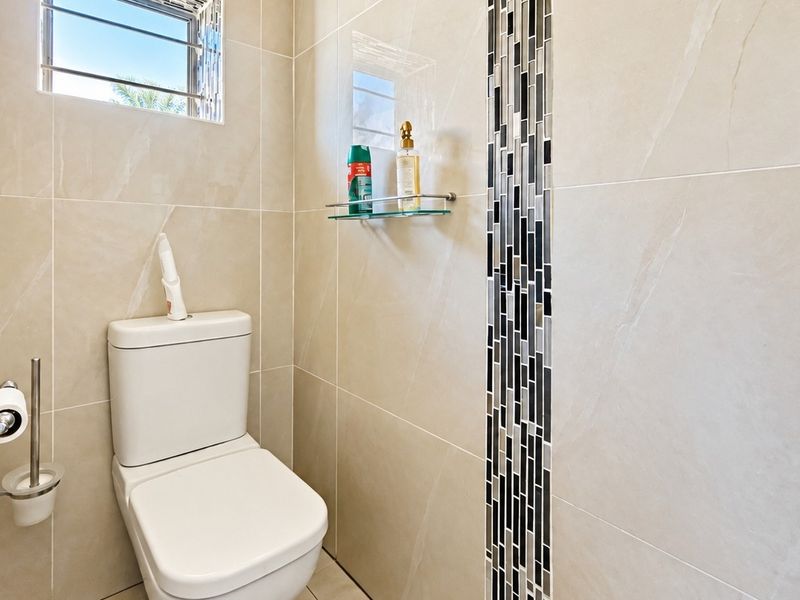 A modern bathroom featuring neutral large-format wall tiles with a vertical mosaic accent strip and a louver window for ventilation.