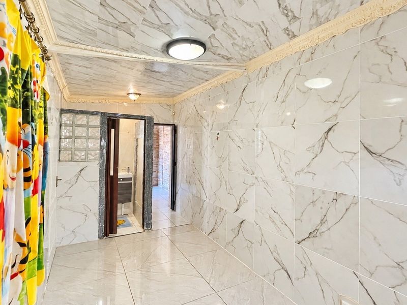 A tiled hallway featuring marble-effect wall and floor tiles, decorative coving, and access to an adjacent bathroom area.