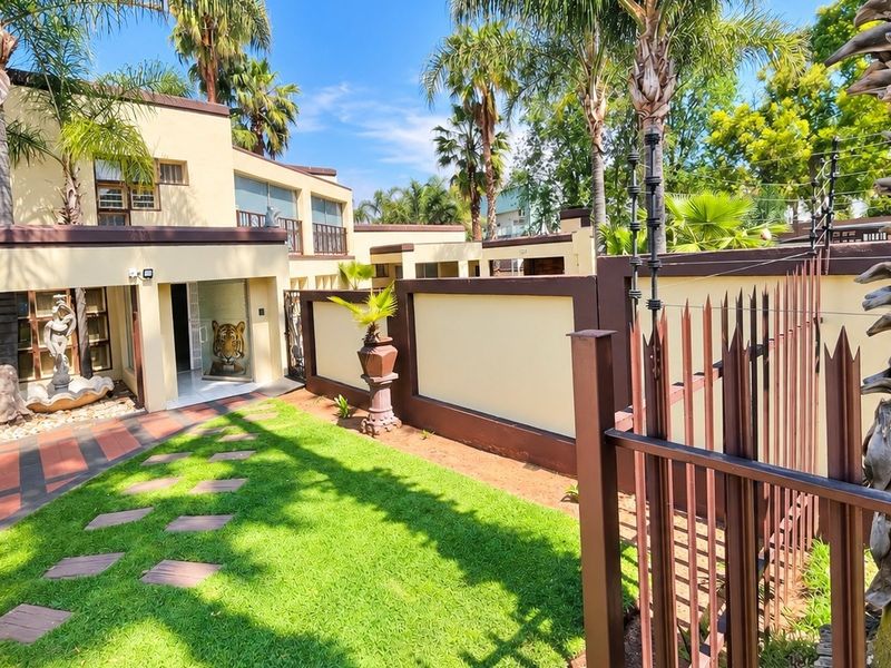Front exterior view of the property featuring a landscaped garden, paved walkway, secure boundary wall with electric fencing, and a covered entrance area.