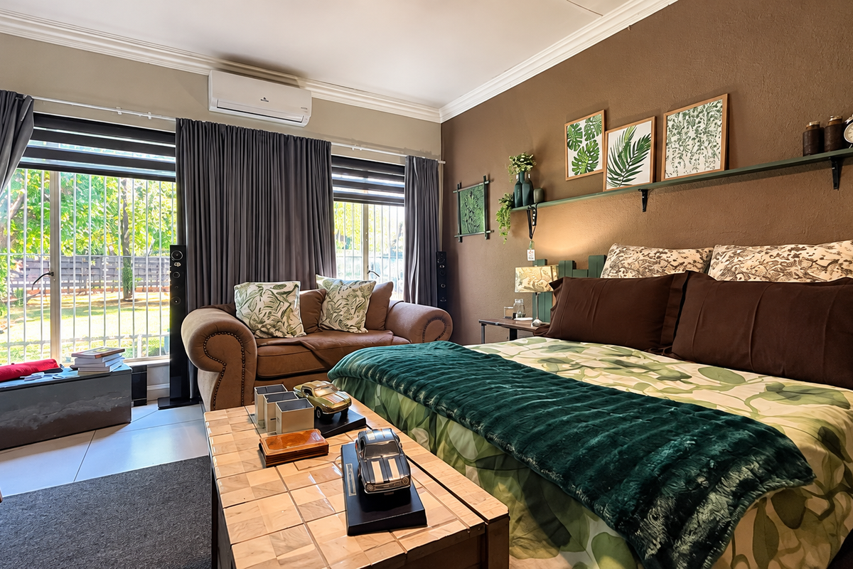 A well-maintained bedroom featuring crown molding, a split-system air conditioner, and large sliding glass doors with security bars providing access to the garden.