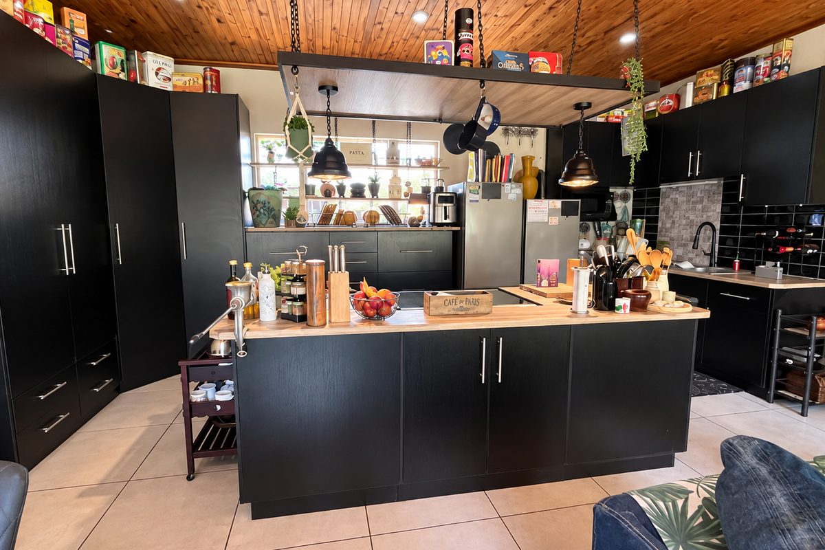Modern kitchen featuring sleek black cabinetry, a central island with a timber benchtop, tiled splashback, and a warm timber-paneled ceiling.