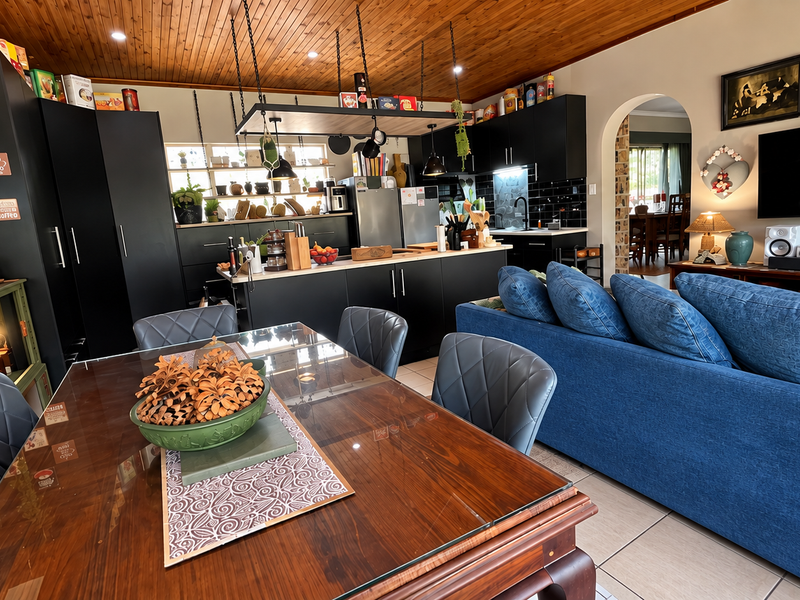 Spacious open-plan living and dining area featuring a modern kitchen with black cabinetry, a central island, and a warm timber-paneled ceiling.