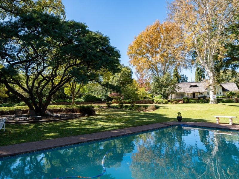 A spacious outdoor pool area featuring a well-maintained swimming pool set within a large, lush garden with mature trees and expansive lawn.