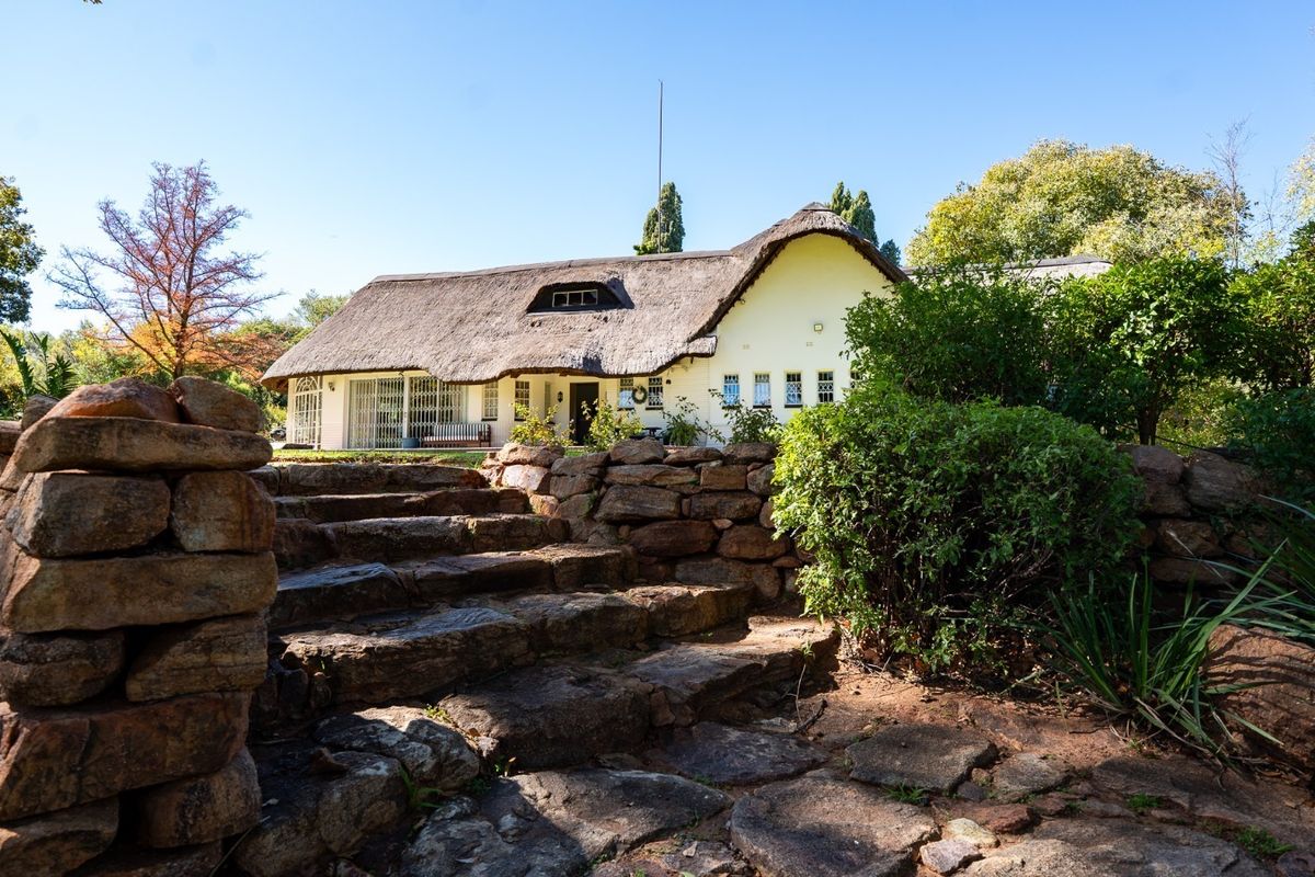 A charming thatched-roof house viewed from the rear garden, featuring natural stone retaining walls and a stone staircase leading to the residence.