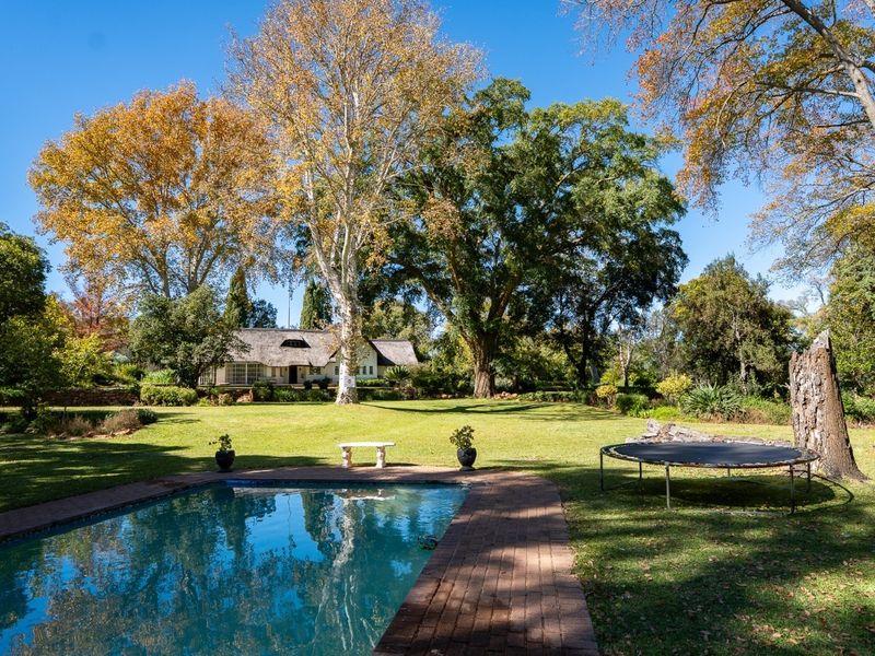 Spacious backyard featuring a swimming pool with brick surround, expansive lawn, and mature trees, offering a serene outdoor setting.