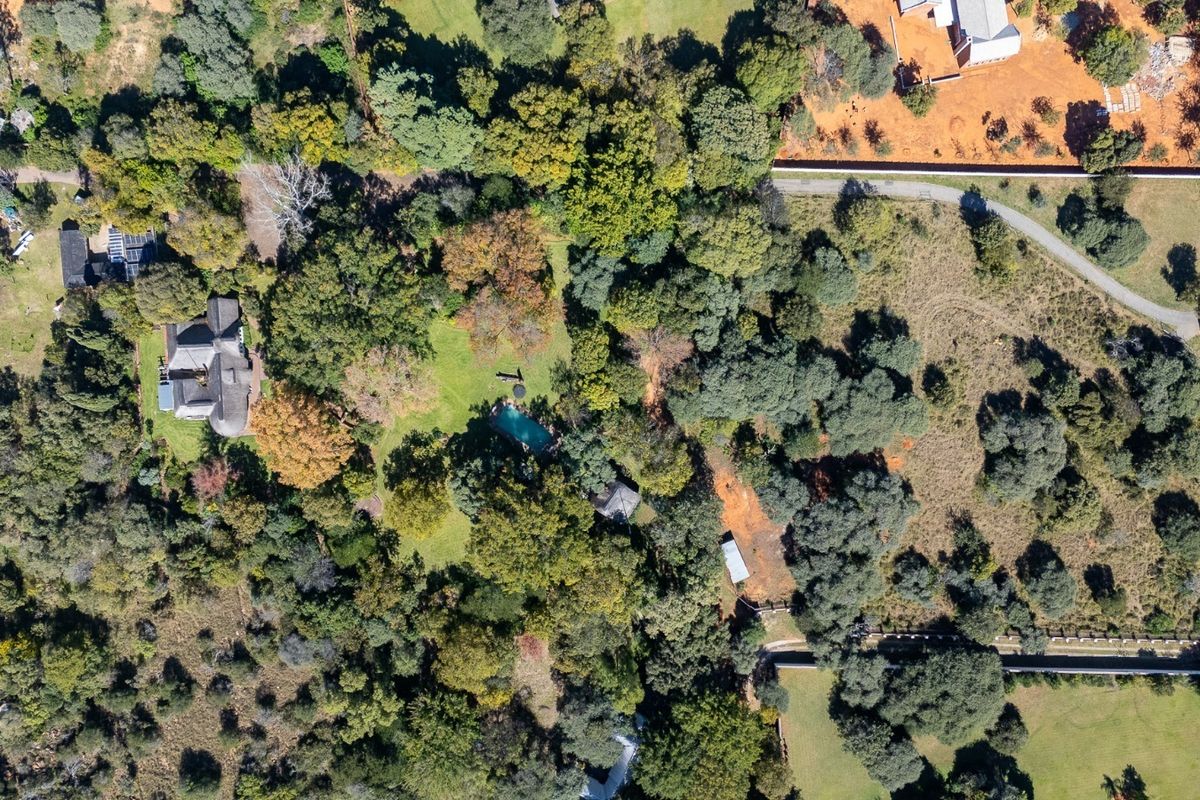 Aerial view of a large residential property featuring a swimming pool, extensive mature trees, and established garden grounds.