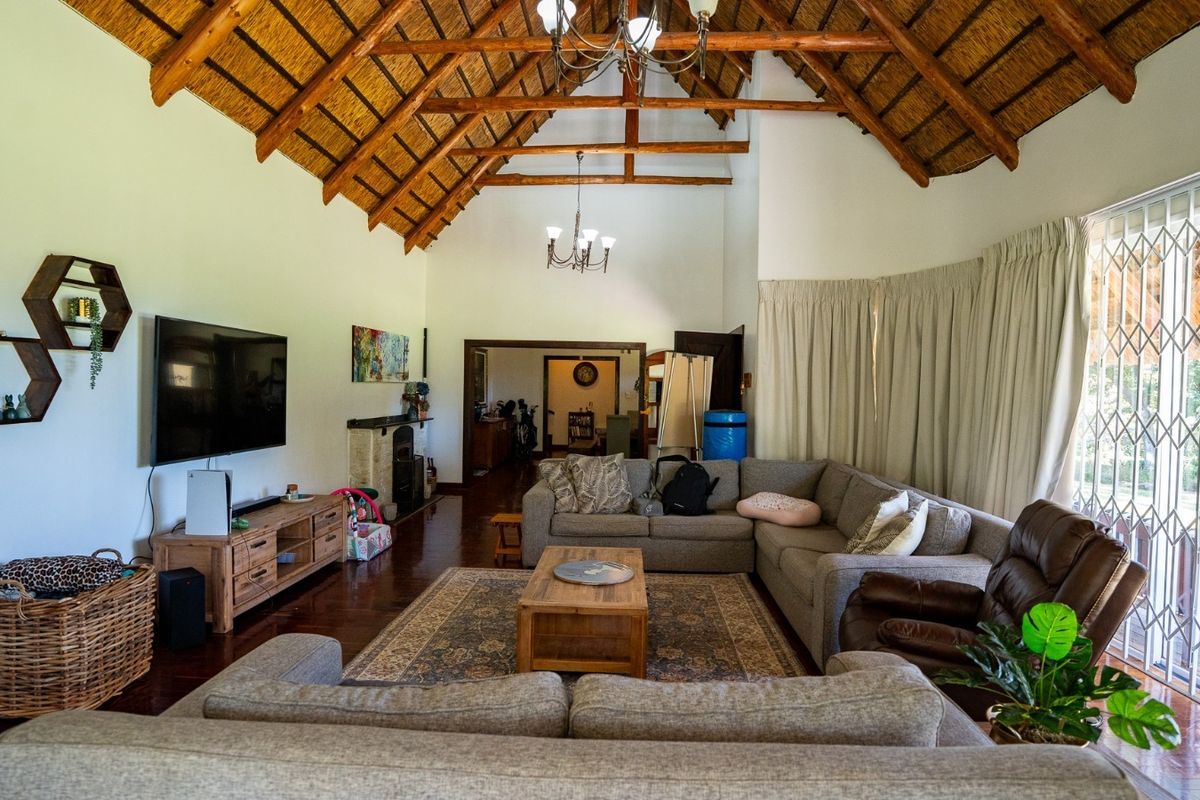 Spacious living room featuring a high vaulted thatched ceiling with exposed timber rafters, hardwood flooring, a fireplace, and large sliding doors with security gates.