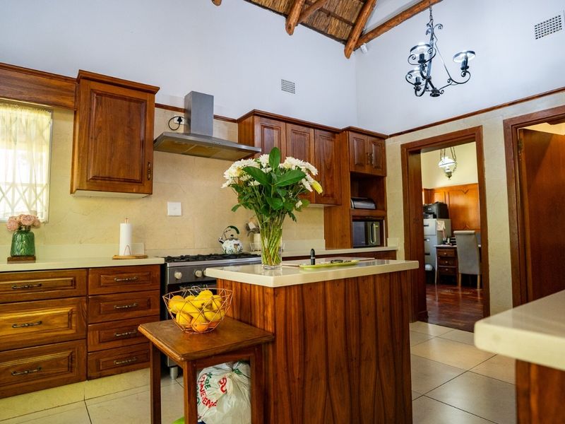 A well-maintained kitchen featuring warm wooden cabinetry, stone countertops, a central island, and a distinctive vaulted thatched ceiling with exposed beams.