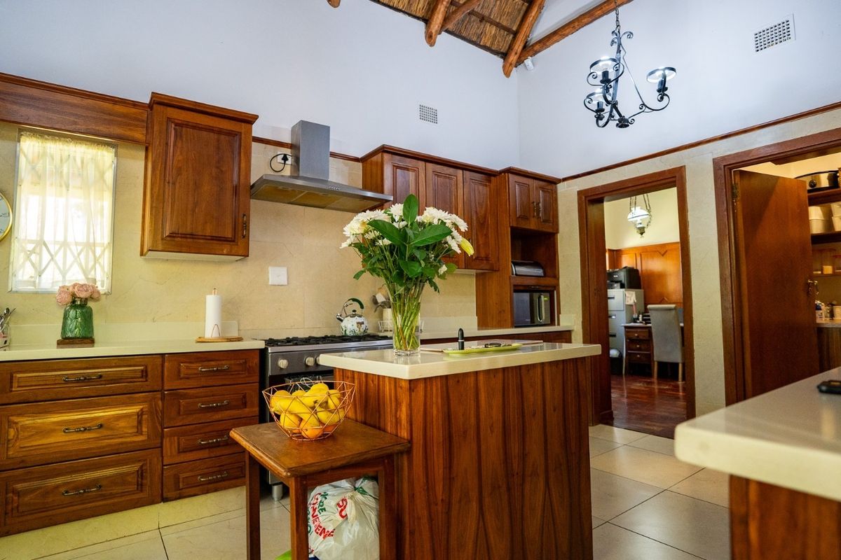 A well-maintained kitchen featuring warm wooden cabinetry, stone countertops, a central island, and a distinctive vaulted thatched ceiling with exposed beams.