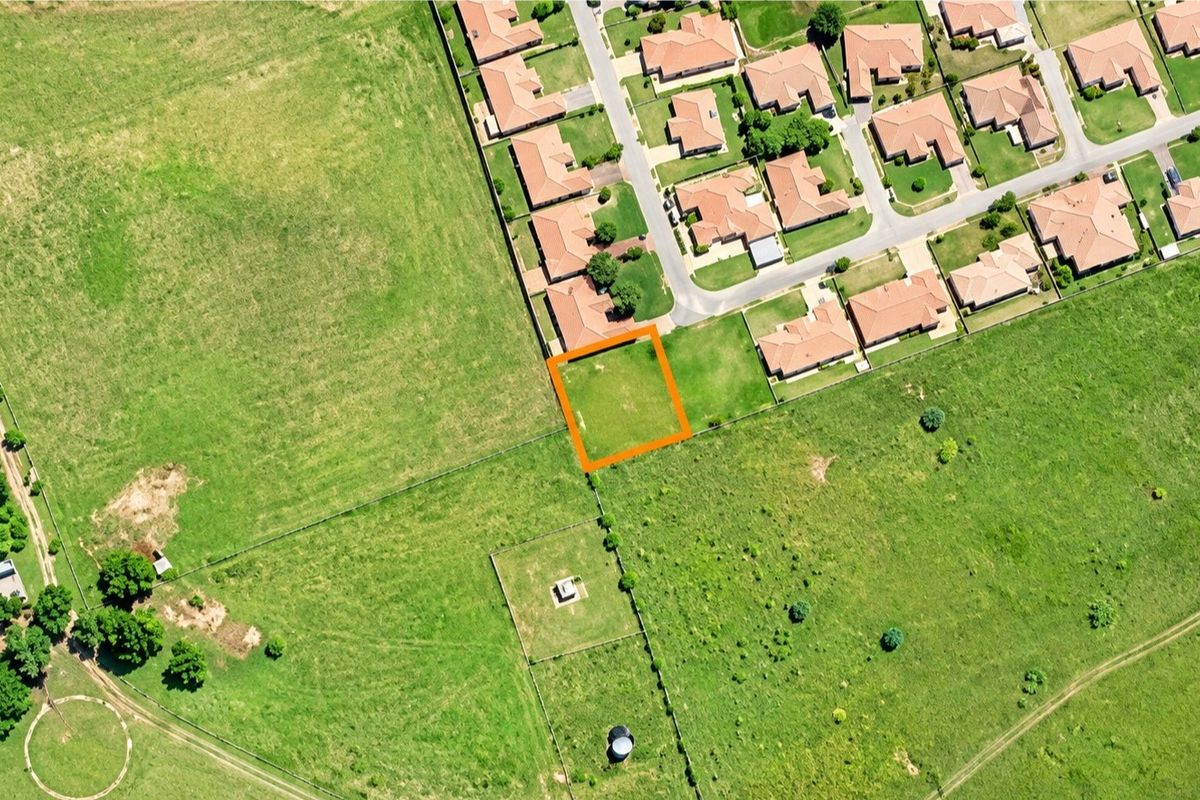 Aerial view of a vacant residential plot highlighted in orange, situated adjacent to an established suburban neighborhood.