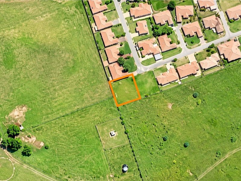 Aerial view of a vacant residential plot highlighted in orange, situated adjacent to an established suburban neighborhood.