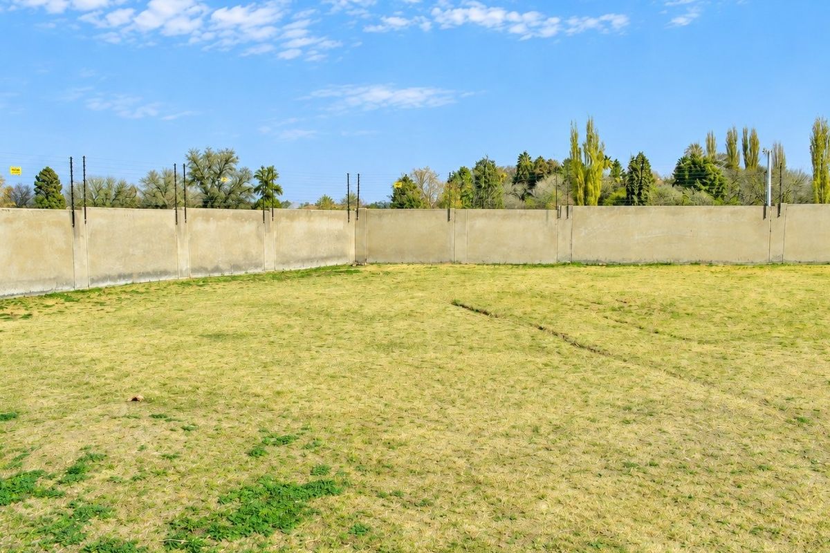 A vacant residential plot featuring a level grassed area enclosed by a perimeter wall with installed electric fencing.