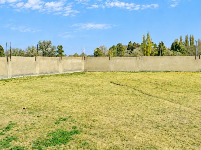 A vacant residential plot featuring a level grassed area enclosed by a perimeter wall with installed electric fencing.