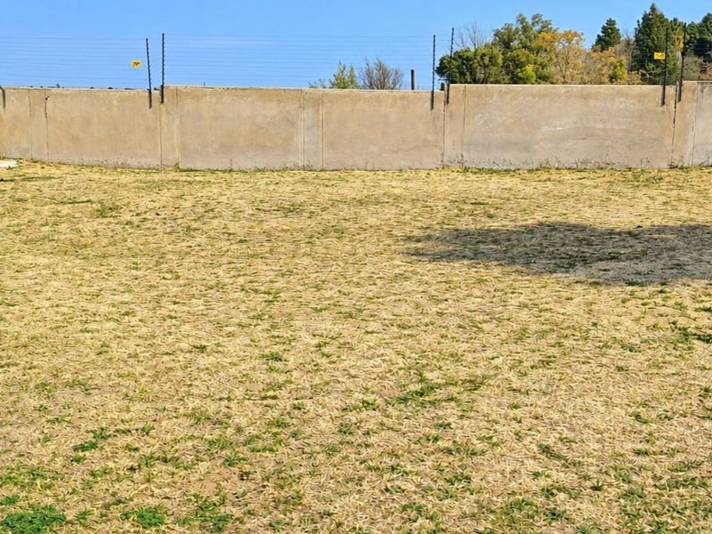 A vacant residential plot featuring a perimeter wall with installed electric fencing and dry grass coverage.