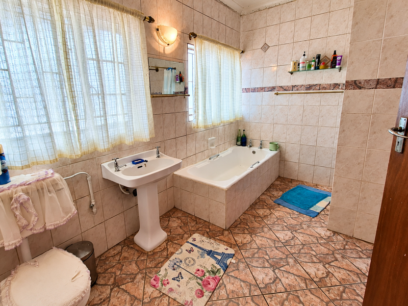 A dated bathroom featuring a pedestal basin, built-in bathtub, and full-height wall tiling. The space requires cosmetic updates to modernize the finishes.