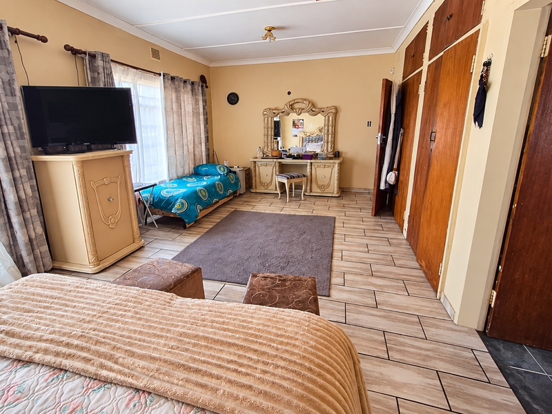 Spacious bedroom featuring tiled flooring and extensive built-in wooden cabinetry, offering ample storage space and a functional layout.