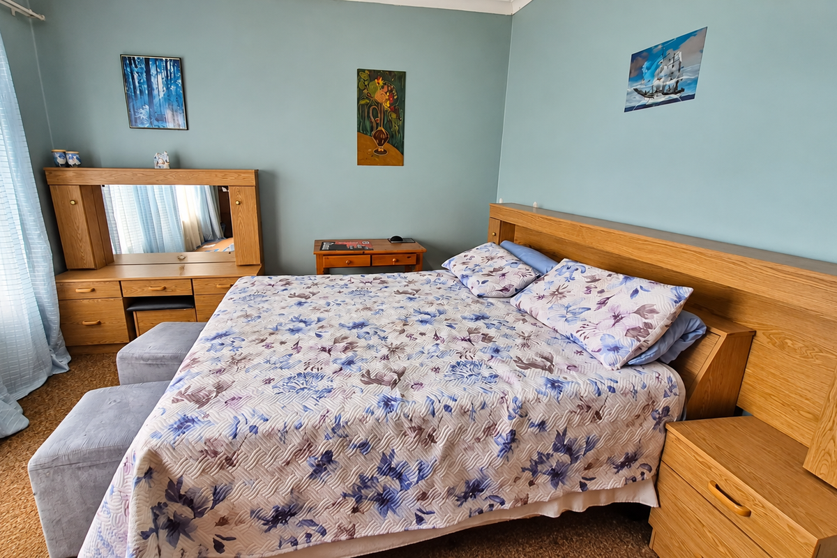 A bedroom featuring a built-in wooden headboard and matching vanity unit, finished with light blue walls and carpeted flooring.