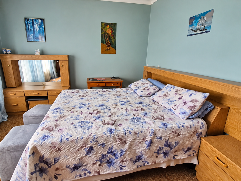 A bedroom featuring a built-in wooden headboard and matching vanity unit, finished with light blue walls and carpeted flooring.