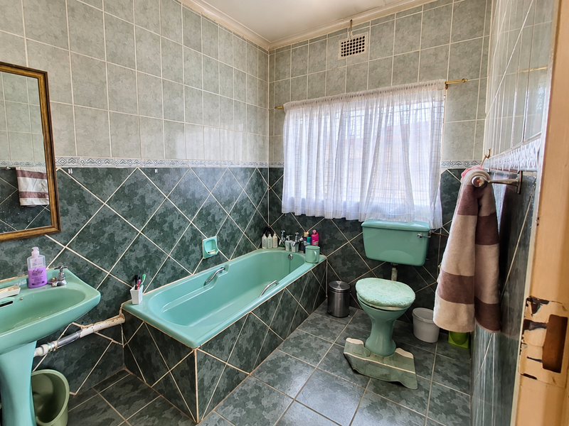 A dated bathroom featuring green sanitaryware, tiled walls and flooring, and a built-in bathtub, offering significant potential for a modern renovation.
