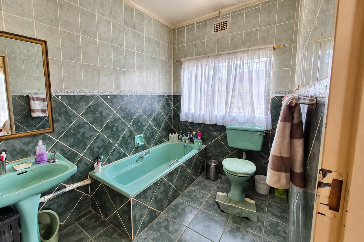 A dated bathroom featuring green sanitaryware, tiled walls and flooring, and a built-in bathtub, offering significant potential for a modern renovation.