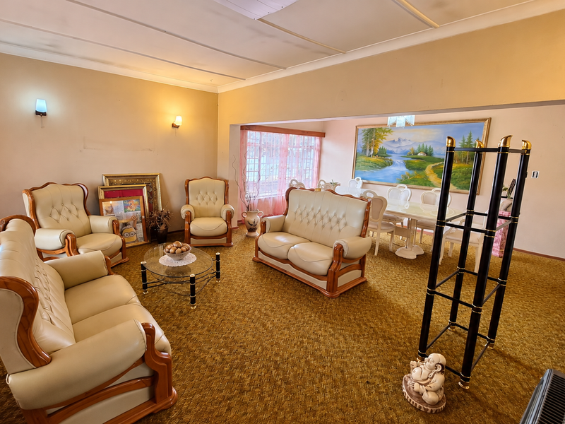 Spacious open-plan living and dining area featuring coved ceilings, wall-mounted lighting, and carpeted flooring, offering a versatile layout for family living.