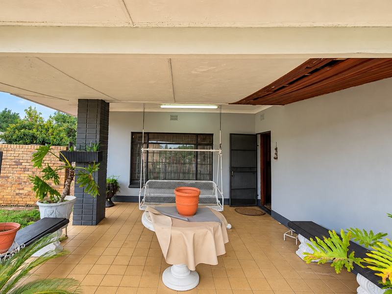 A covered patio area featuring tiled flooring, brick columns, and a timber-paneled ceiling section, providing a functional outdoor entertainment space.