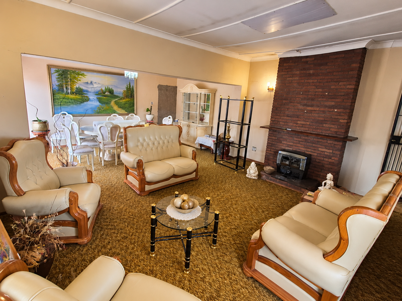Open plan living and dining area featuring a prominent brick fireplace, coved ceilings, and dated carpet flooring throughout the space.