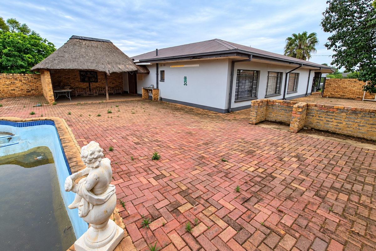 Rear exterior view featuring a swimming pool, brick-paved patio area, and a thatched lapa with built-in braai facilities.