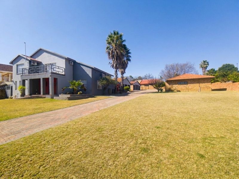 Spacious front exterior view featuring a large lawn, paved driveway, multi-car garage, and a two-story residence with a balcony.