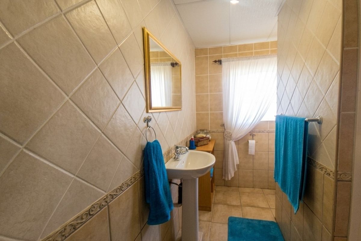 A functional bathroom featuring a pedestal sink, neutral ceramic wall and floor tiling, and a window for natural light.