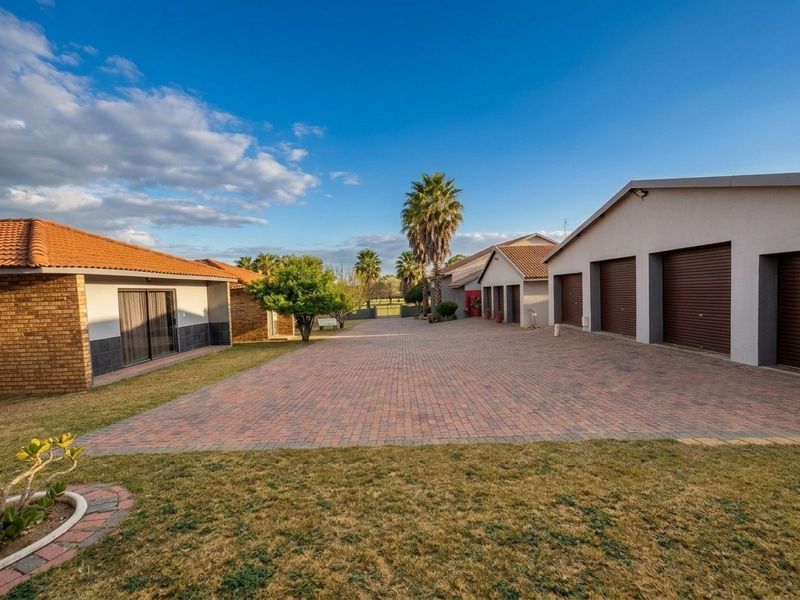 Spacious paved driveway leading to multiple garage units, featuring well-maintained brick and plaster exterior finishes with a tiled roof.