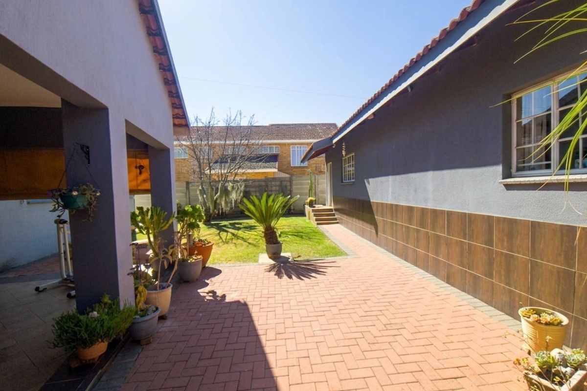 A rear exterior view featuring a paved patio area, covered walkway, and a well-maintained garden space between two building sections.