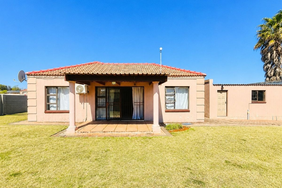 Rear view of a townhouse featuring a covered patio, tiled roof, and a spacious lawn area.