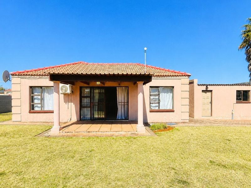 Rear view of a townhouse featuring a covered patio, tiled roof, and a spacious lawn area.