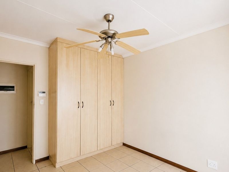 A clean, empty bedroom featuring light-toned built-in cupboards, tiled flooring, and a ceiling fan, offering a neutral canvas for personalization.