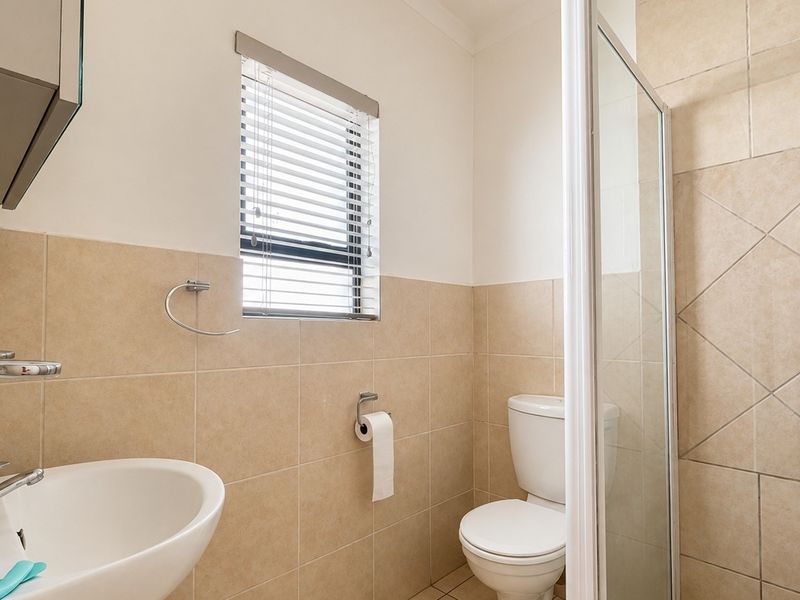 A functional bathroom featuring a pedestal basin, a glass-enclosed shower, and neutral wall tiling with a window for natural light.