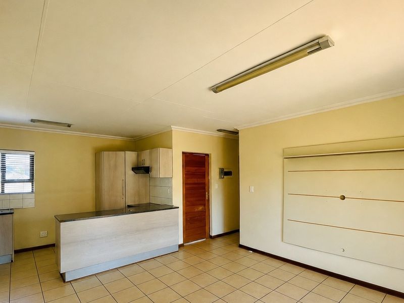 An open-plan living and kitchen area featuring tiled flooring, built-in cabinetry, an island, and an air conditioning unit in a neutral, vacant space.