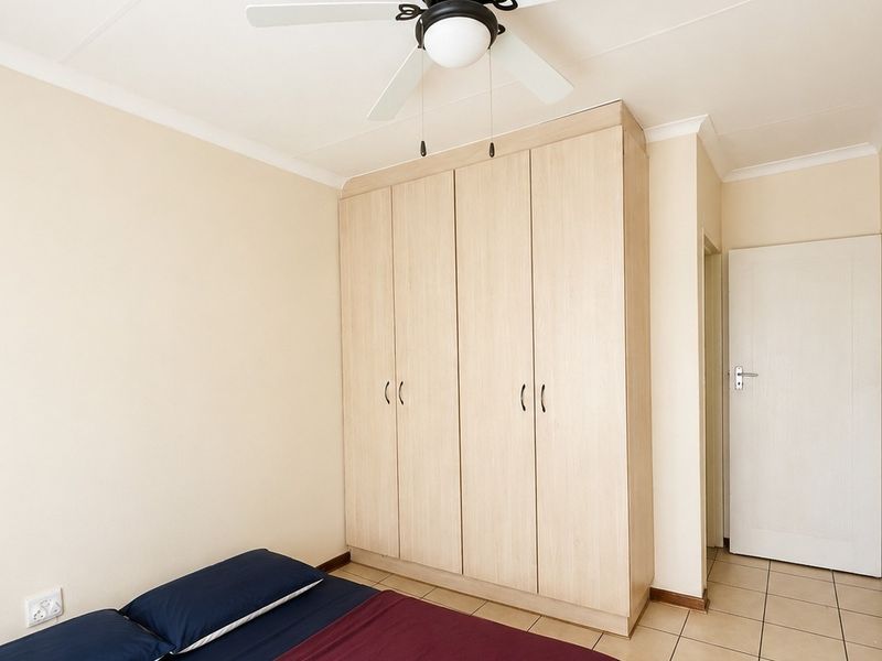 A well-maintained bedroom featuring light wood-finish built-in wardrobes, tiled flooring, and a ceiling fan, offering a clean and functional living space.