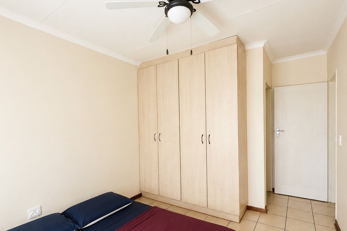 A well-maintained bedroom featuring light wood-finish built-in wardrobes, tiled flooring, and a ceiling fan, offering a clean and functional living space.