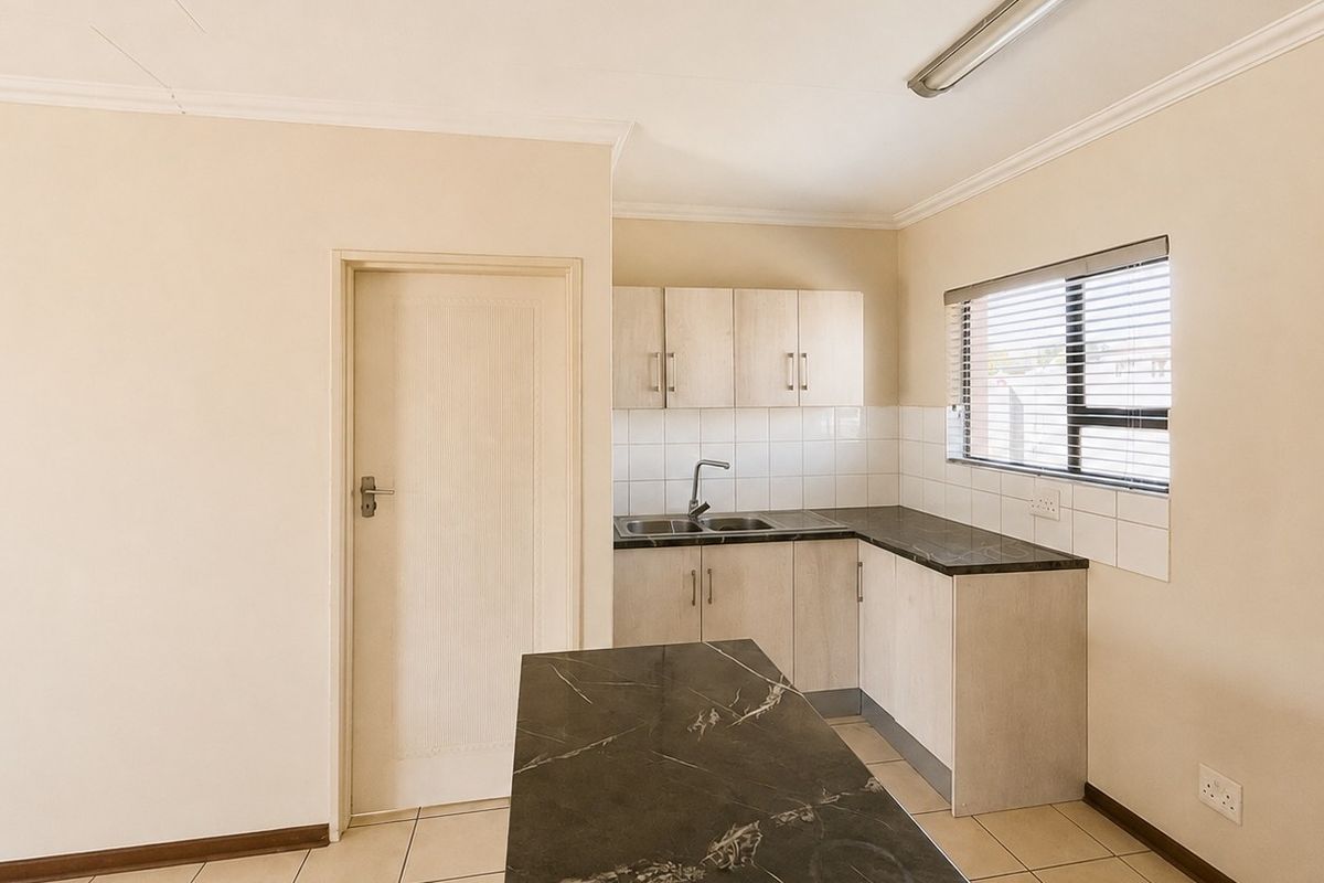A functional kitchen area featuring laminate cabinetry, dark countertops, a stainless steel sink, and tiled flooring, offering a clean and neutral space.