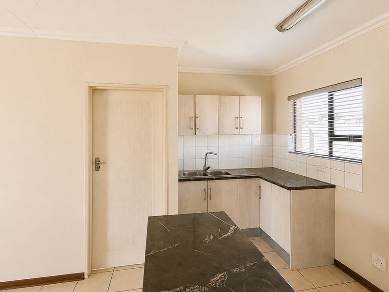 A functional kitchen area featuring laminate cabinetry, dark countertops, a stainless steel sink, and tiled flooring, offering a clean and neutral space.