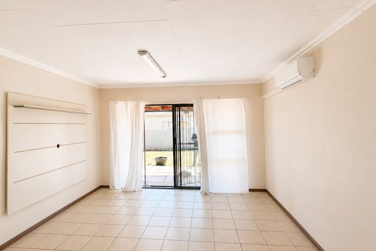 A bright, empty living room featuring tiled floors, a wall-mounted air conditioning unit, and sliding glass doors leading to an outdoor patio area.
