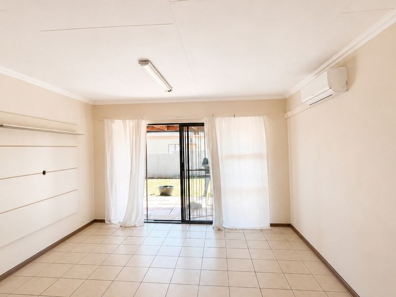 A bright, empty living room featuring tiled floors, a wall-mounted air conditioning unit, and sliding glass doors leading to an outdoor patio area.