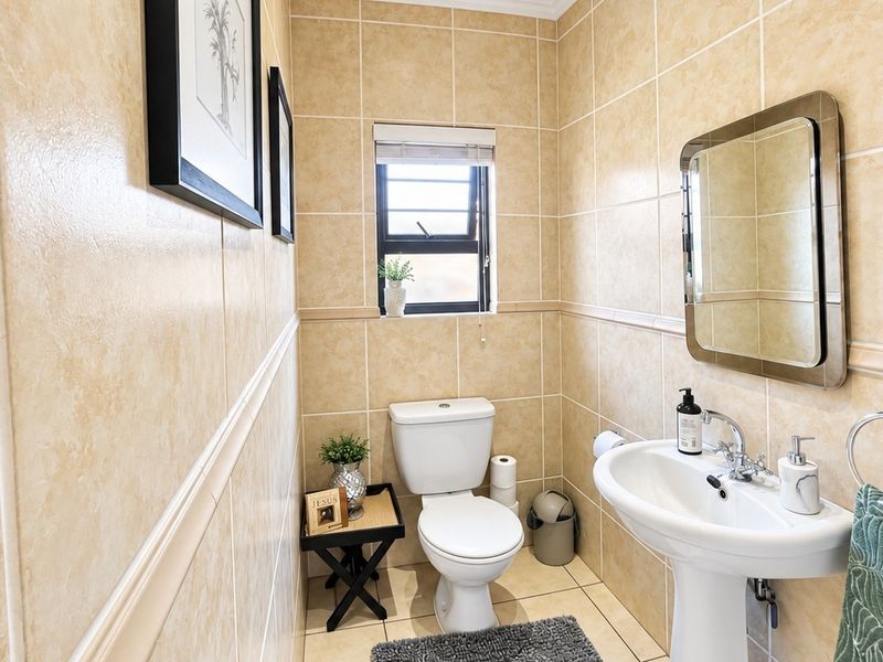 A compact guest bathroom featuring neutral ceramic wall and floor tiles, a pedestal basin, and a standard toilet.