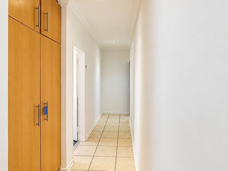 A clean and bright hallway featuring neutral tiled flooring, recessed downlighting, and integrated floor-to-ceiling wooden cabinetry for ample storage.